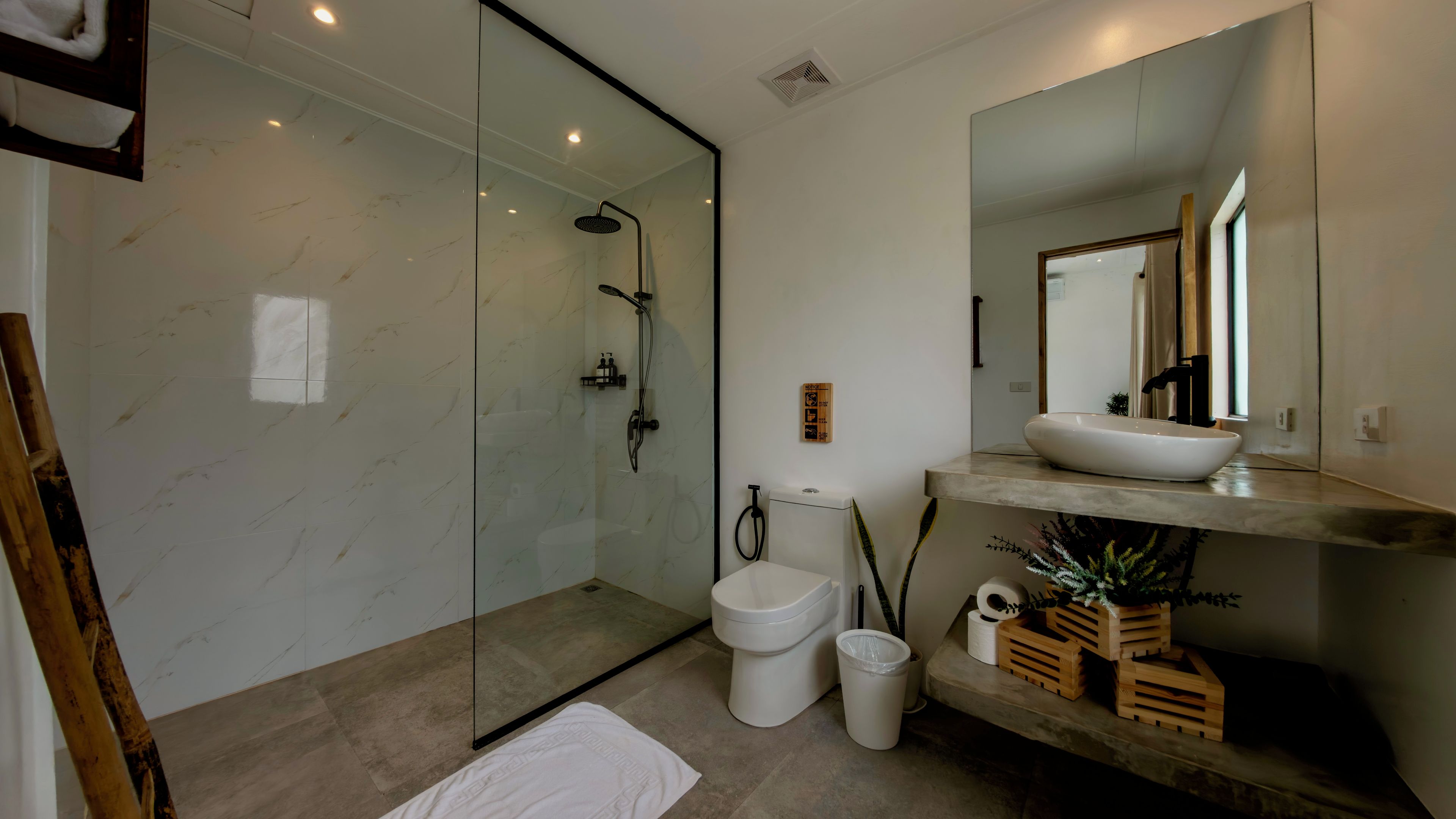 A modern bathroom with a glass-enclosed shower, a toilet, and a sink with a mirror above.