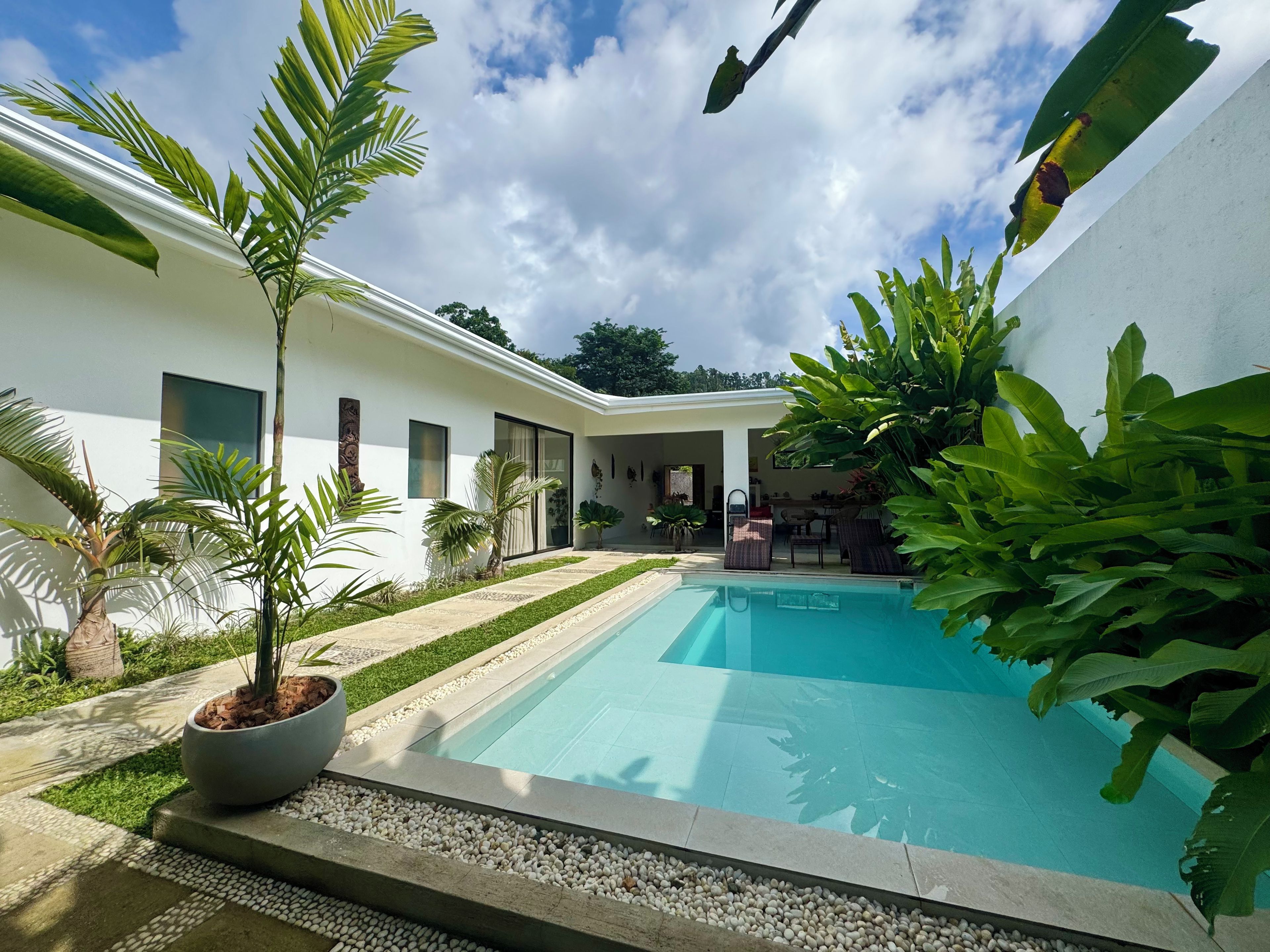 A modern pool area with a clear blue pool, surrounded by potted plants and a white building with large windows.