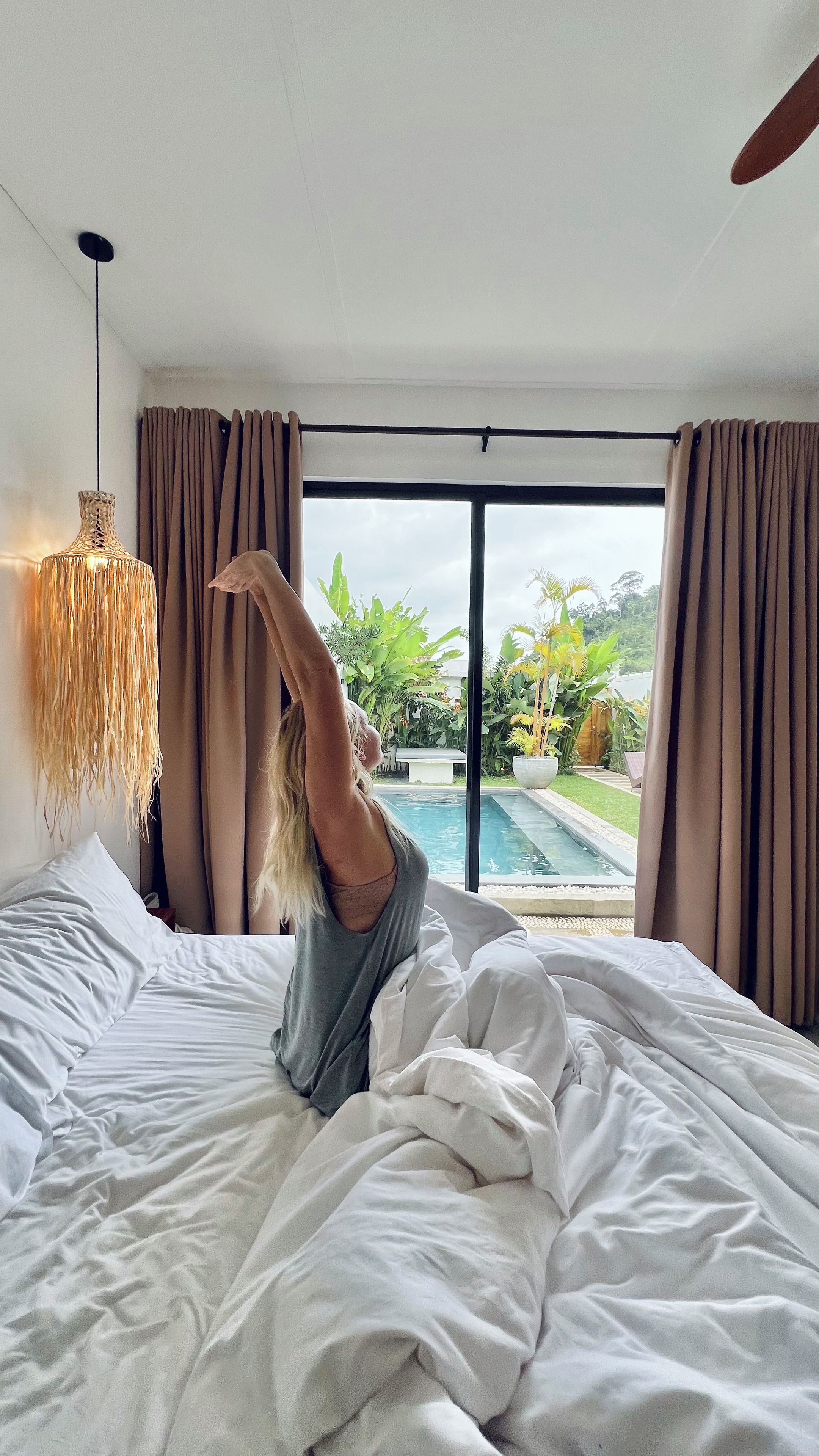A bedroom with a large bed, a view of a swimming pool, and curtains.