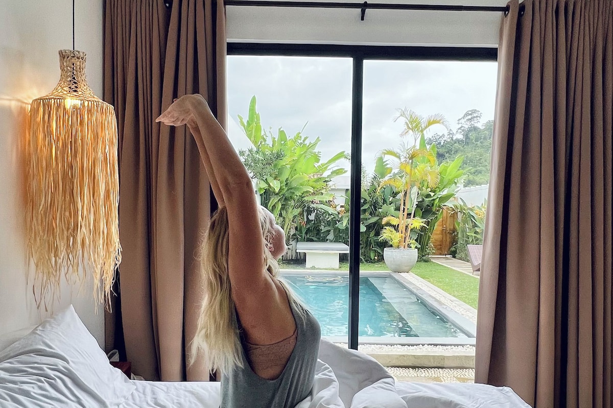 A bedroom with a large bed, a view of a swimming pool, and curtains.