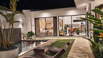 A modern house with a swimming pool, outdoor seating, and a well-lit interior.