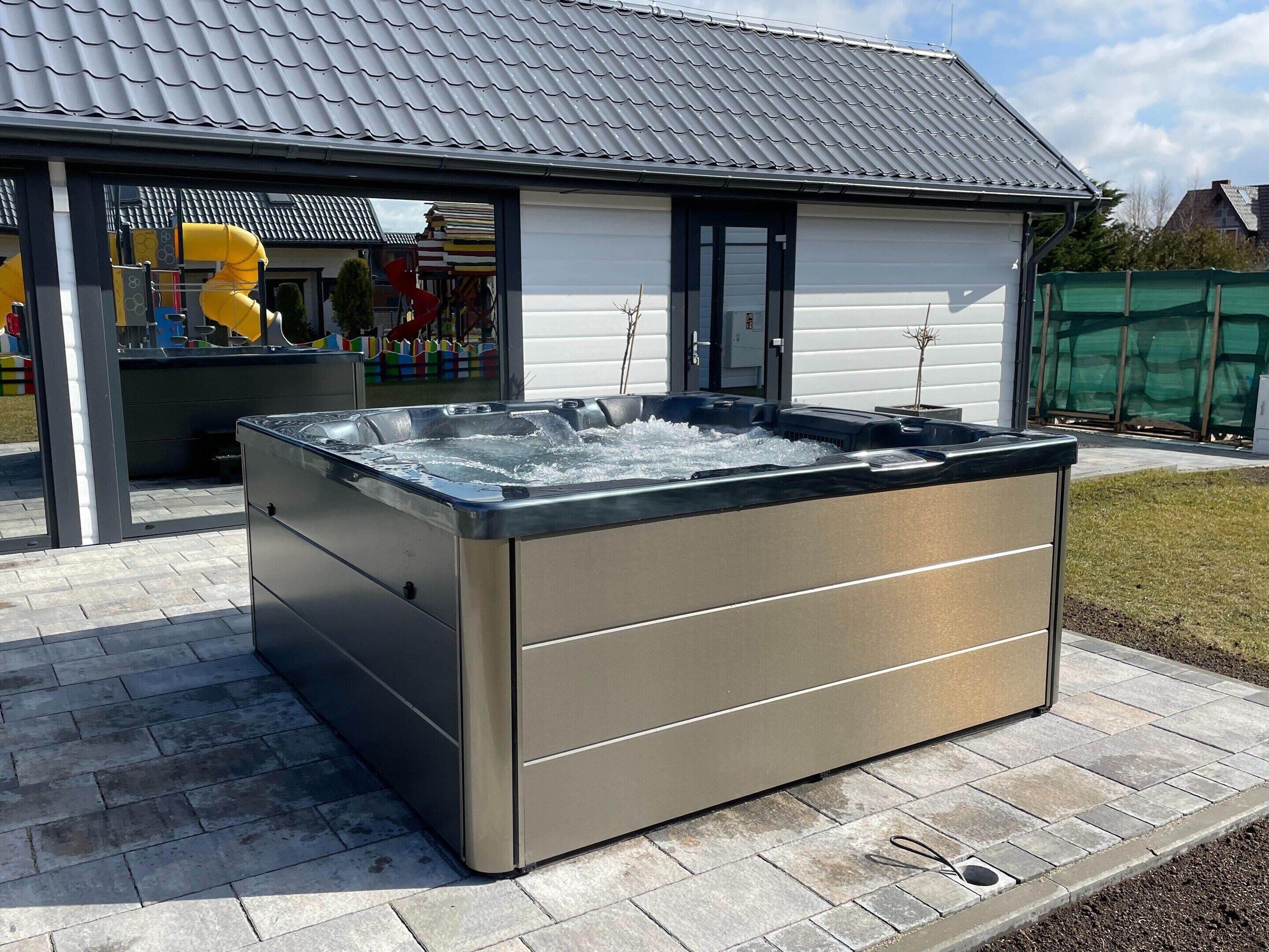 Un grand jacuzzi extérieur situé dans un espace patio, avec un sol carrelé et un bâtiment en arrière-plan.