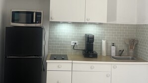 Une cuisine de taille réduite, avec des meubles blancs, un four à micro-ondes, une machine à café et un évier.