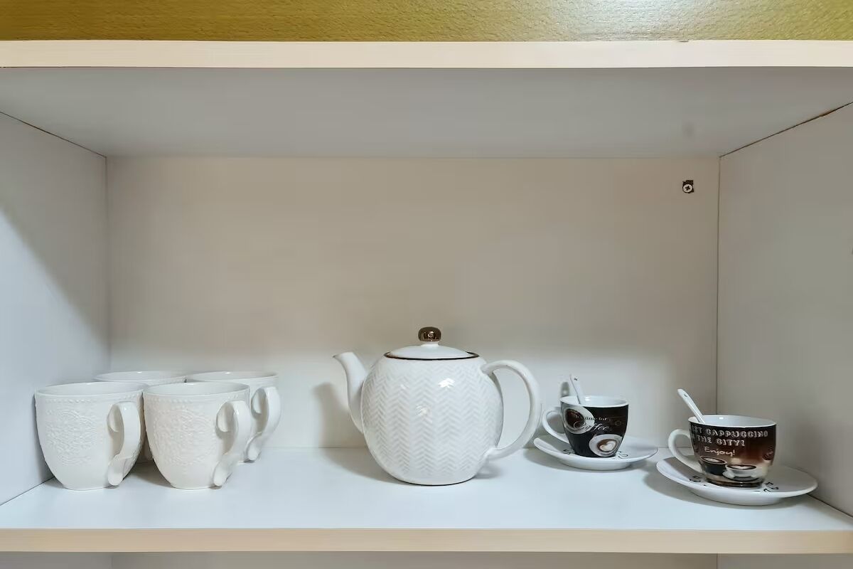 A white shelf with a white teapot, four white cups, and two saucers with a cup and saucer.
