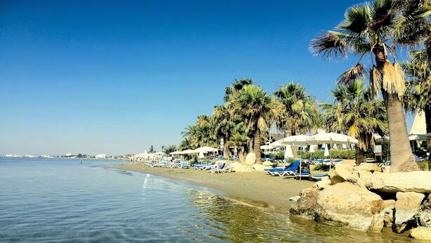 Ein Strand mit klarem Wasser, Palmen und Liegestühlen.