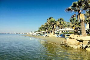 Een strand met helder water, palmbomen en ligbedden.