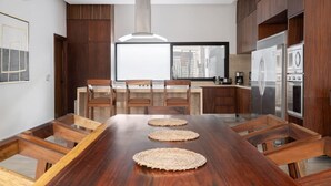A modern kitchen with a wooden dining table, built-in appliances, and a large window offering a city view. - Villa Amalia, 5 bdr w/Private Pool in Aldea  Zama (Tulum)