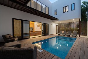 Ein moderner Poolbereich im Freien mit Holzterrasse, Liegestühlen und einem gläsernen Wohnraum.