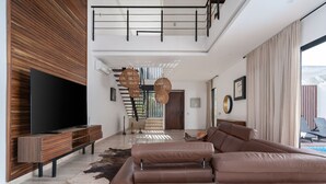 A modern living room with a large sectional sofa, a flat-screen TV, and a staircase leading to an upper level. - Villa Amalia, 5 bdr w/Private Pool in Aldea  Zama (Tulum)