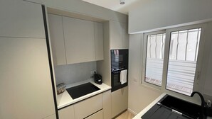 A modern kitchen with grey cabinets, a black countertop, and a window with blinds. - Charming apartment with terrace, village on foot (Valbonne)