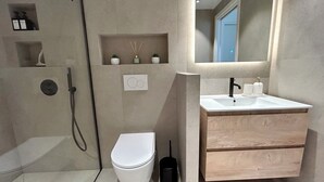A modern bathroom with a walk-in shower, a toilet, a sink with a mirror, and a small shelf with toiletries. - Charming apartment with terrace, village on foot (Valbonne)
