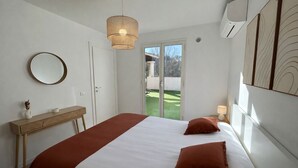 A bedroom with a bed, a bedside table, a mirror, and a view of a green outdoor area through a sliding door. - Charming apartment with terrace, village on foot (Valbonne)