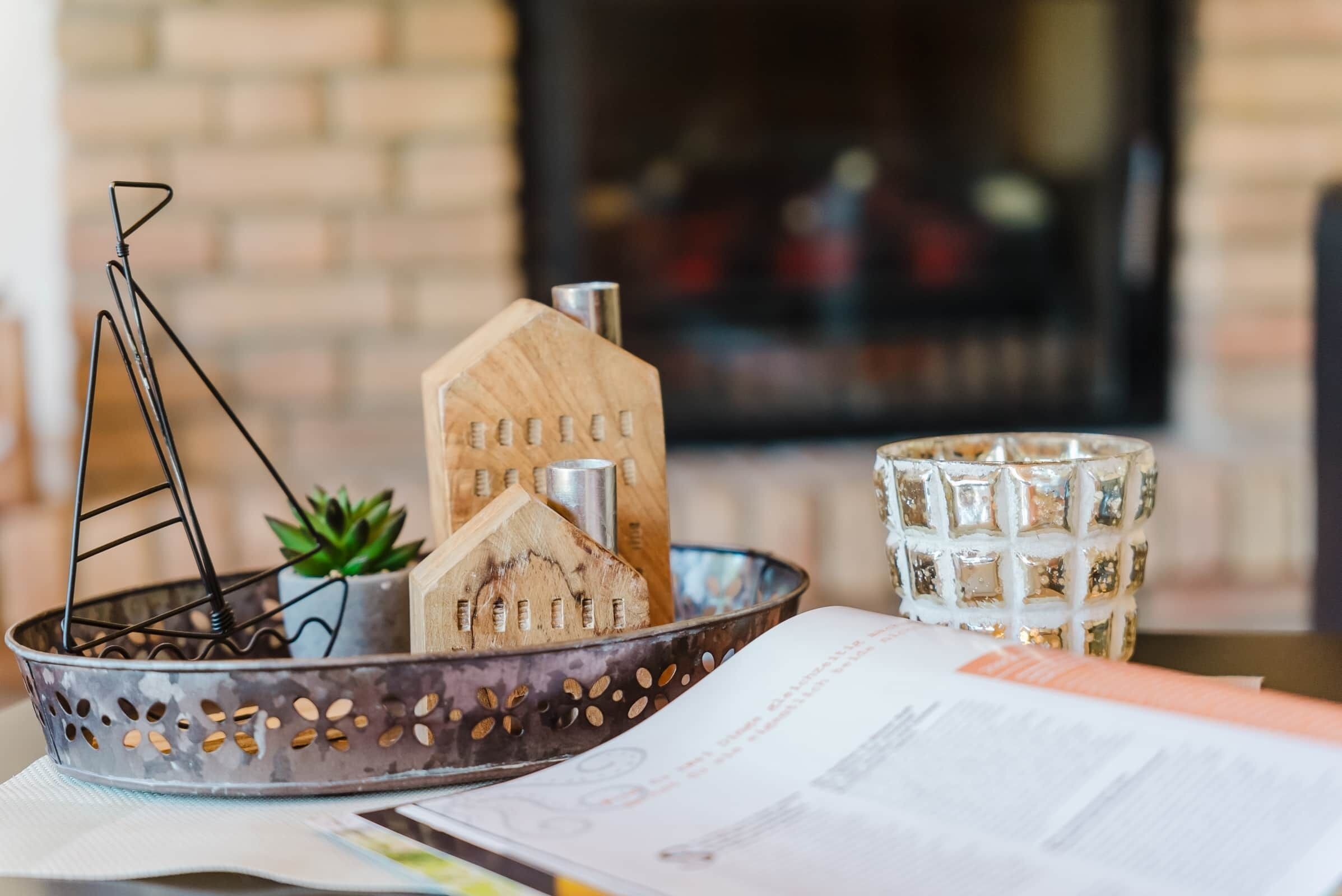 A metal tray with house-shaped objects, a small plant, and a glass with a textured pattern.