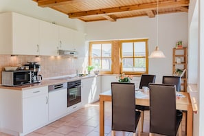 Una cocina moderna con armarios blancos, techo de madera y un comedor con mesa y sillas.