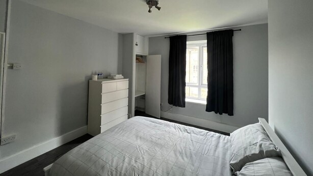 A bedroom with a bed, a dresser, a wardrobe, a window with curtains, and a ceiling fan. - Vauxhall Central Room 3 (Greater London)