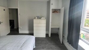 A bedroom with a bed, a white dresser, a closet with a wooden hanger, and a window with a view of buildings. - Vauxhall Central Room 3 (Greater London)