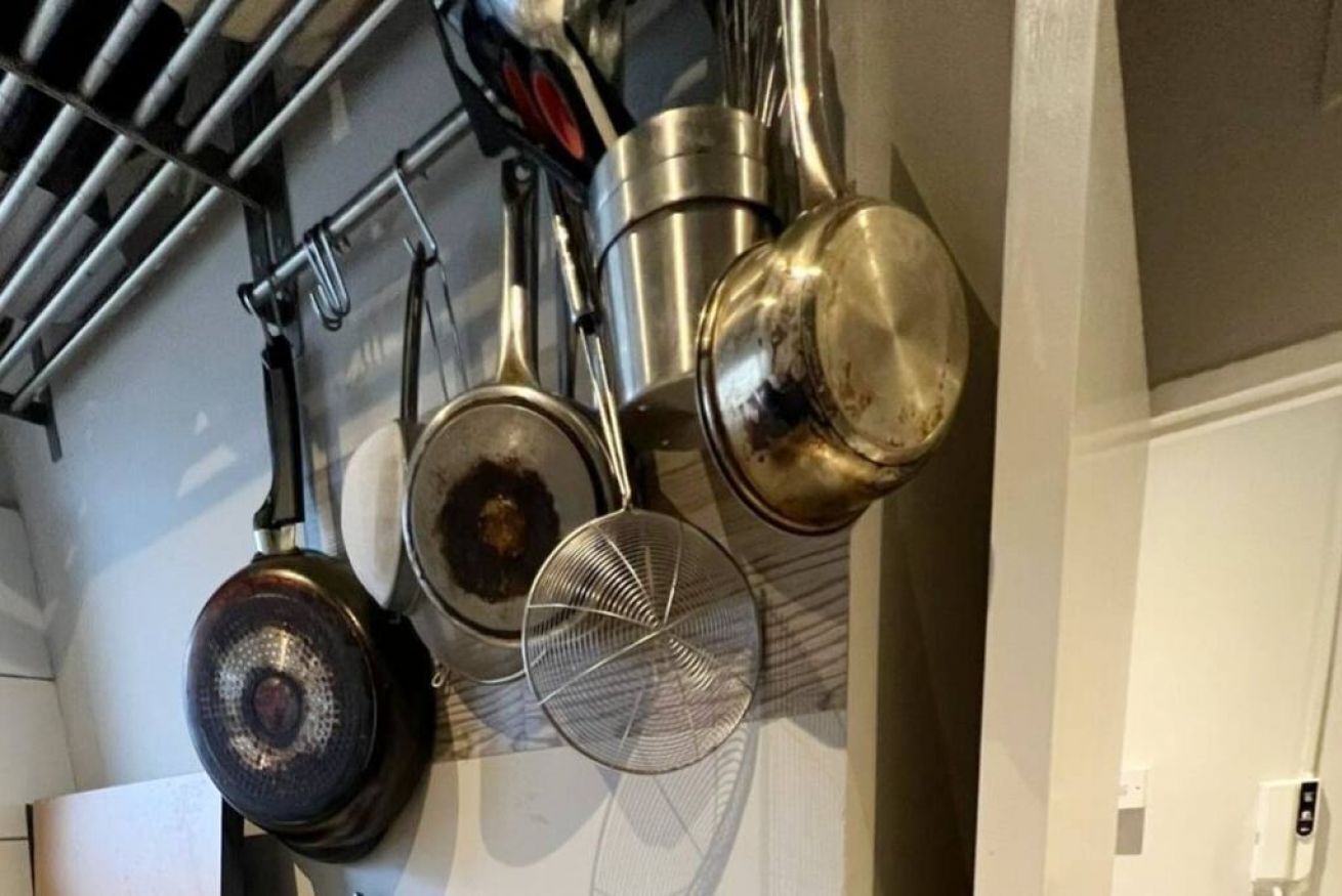 Una cucina con pentole e padelle appese, un colino e un fornello.