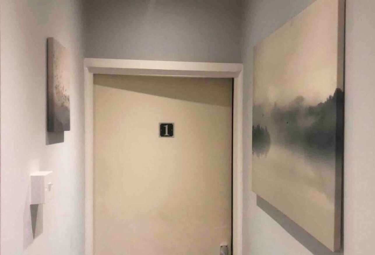 A hallway with a door marked '1', a light switch, and a painting on the wall.