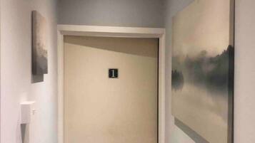 A hallway with a door marked '1', a light switch, and a painting on the wall.