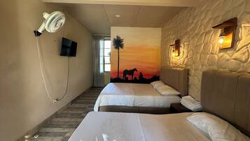 A hotel room with two beds, a ceiling fan, a TV, a sunset mural, and a stone wall.