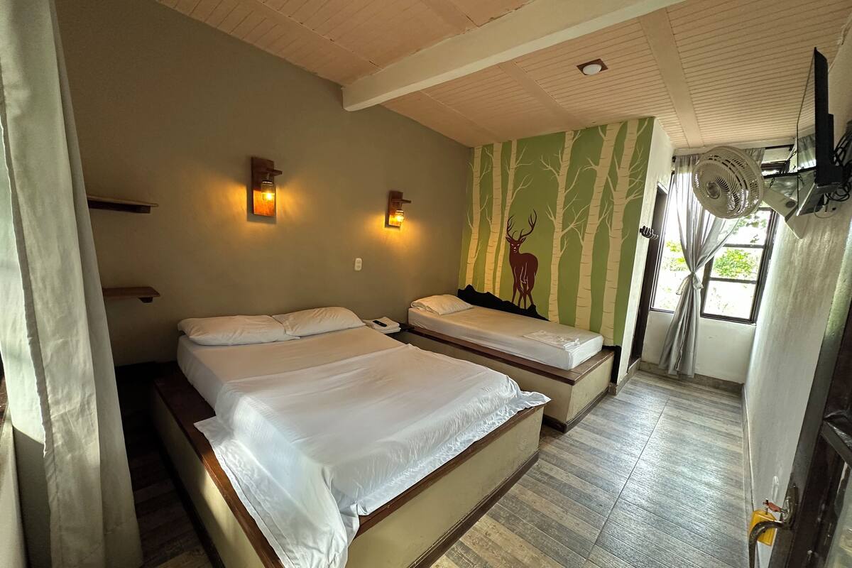 A room with two beds, a wall-mounted fan, and a window with curtains.