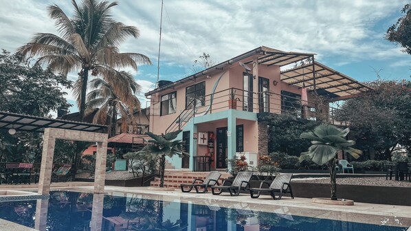 Um edifício de dois andares com piscina, palmeiras e área de estar externa.