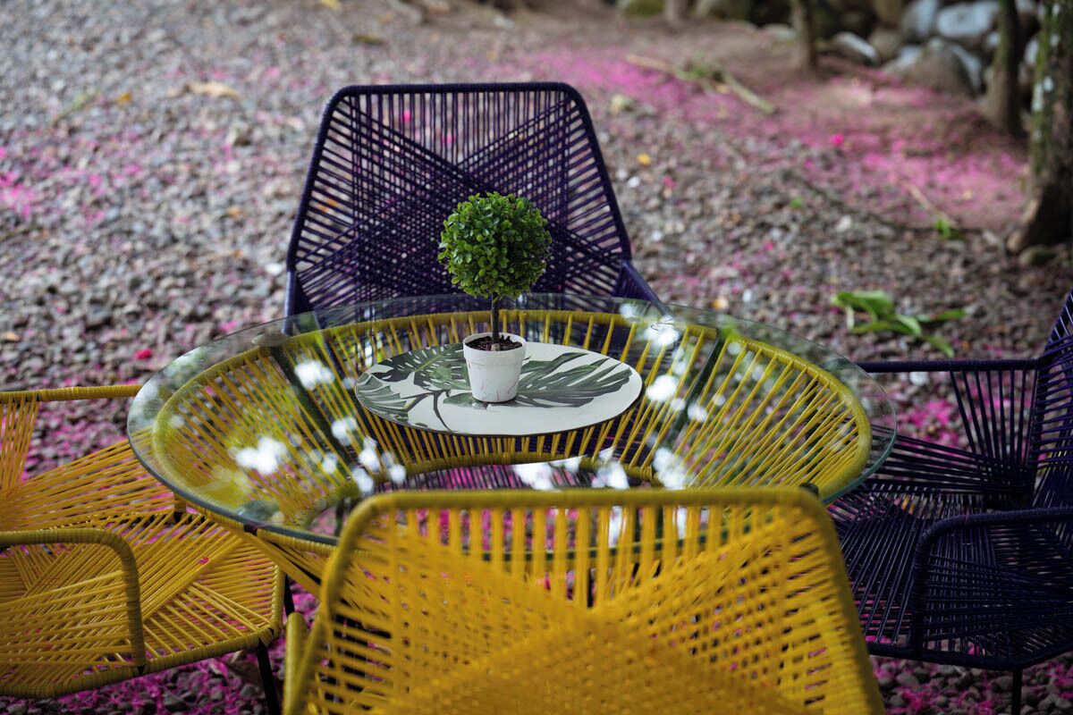 A round glass table with a potted plant and a white mug. Surrounding the table are yellow and black wicker chairs.