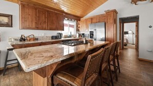 A spacious kitchen with wooden cabinets, a large island with seating, and a rustic ceiling. - Lakeside Cottage, Charming 3-BDRM Retreat W Hottub (Big Bear Lake)
