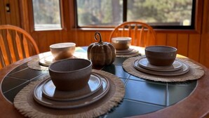 Une table à manger avec quatre bols et une décoration centrale en forme de citrouille, placée devant un mur lambrissé en bois, avec une fenêtre donnant sur une forêt.