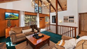 Un salon chaleureux avec un plafond en bois, une grande télévision, une cheminée et un escalier.