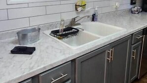 A modern kitchen with grey cabinets, a white countertop, and a large window above the sink.