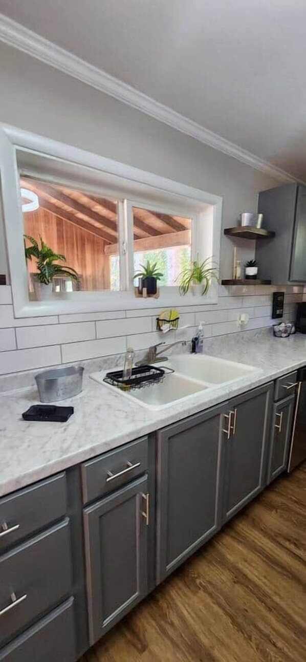 A modern kitchen with grey cabinets, a white countertop, and a large window above the sink.