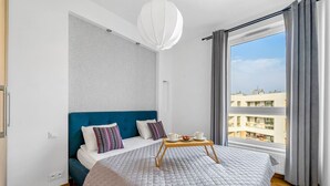 A modern hotel room with a large bed, a view of the city, and a breakfast setup on the bed.