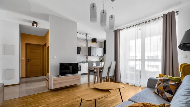 A modern living room with a sofa, a coffee table, a TV, and a dining area with chairs and a table.