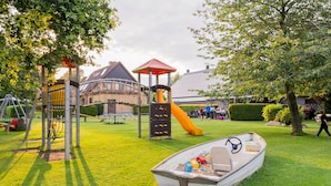 A playground with a slide and climbing structures, a boat filled with toys, and a building in the background. - Vacation apartment half-timbered house "Westen oben" - Bauernhof Hopp (Fehmarn)