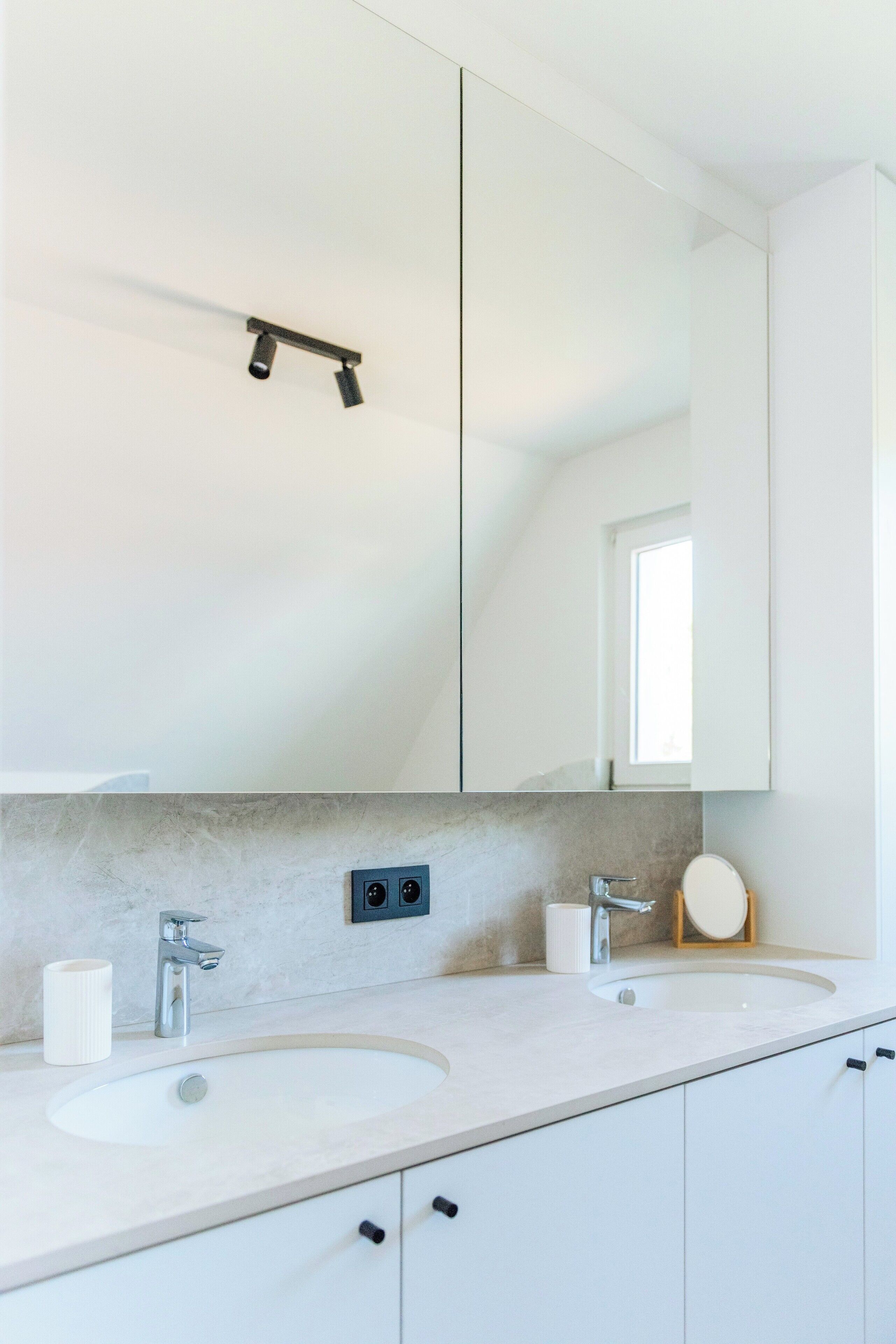 A modern bathroom with two sinks, a large mirror, and a towel rack.