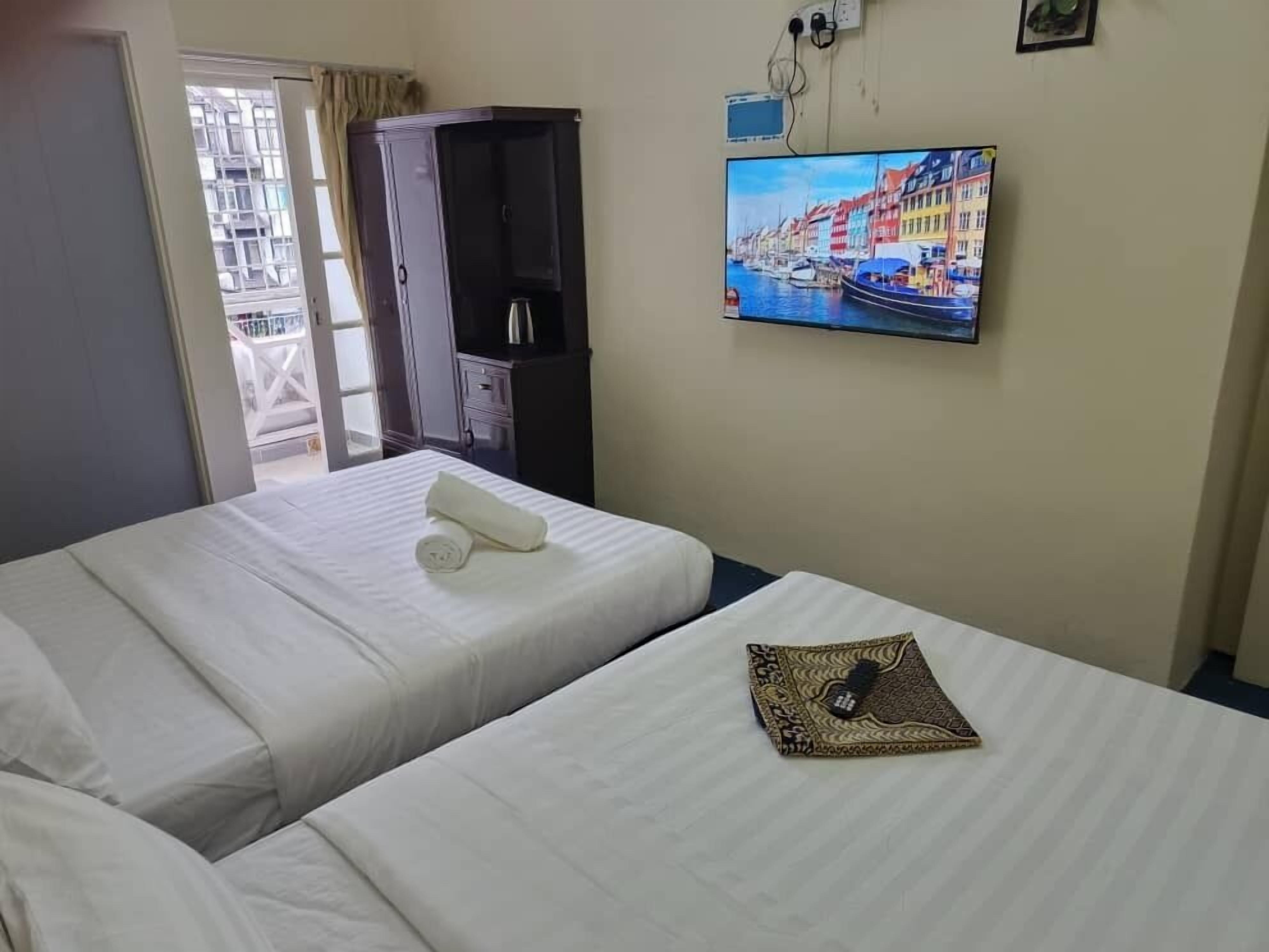 Una camera d'albergo con due letti, una TV a parete e un armadio.