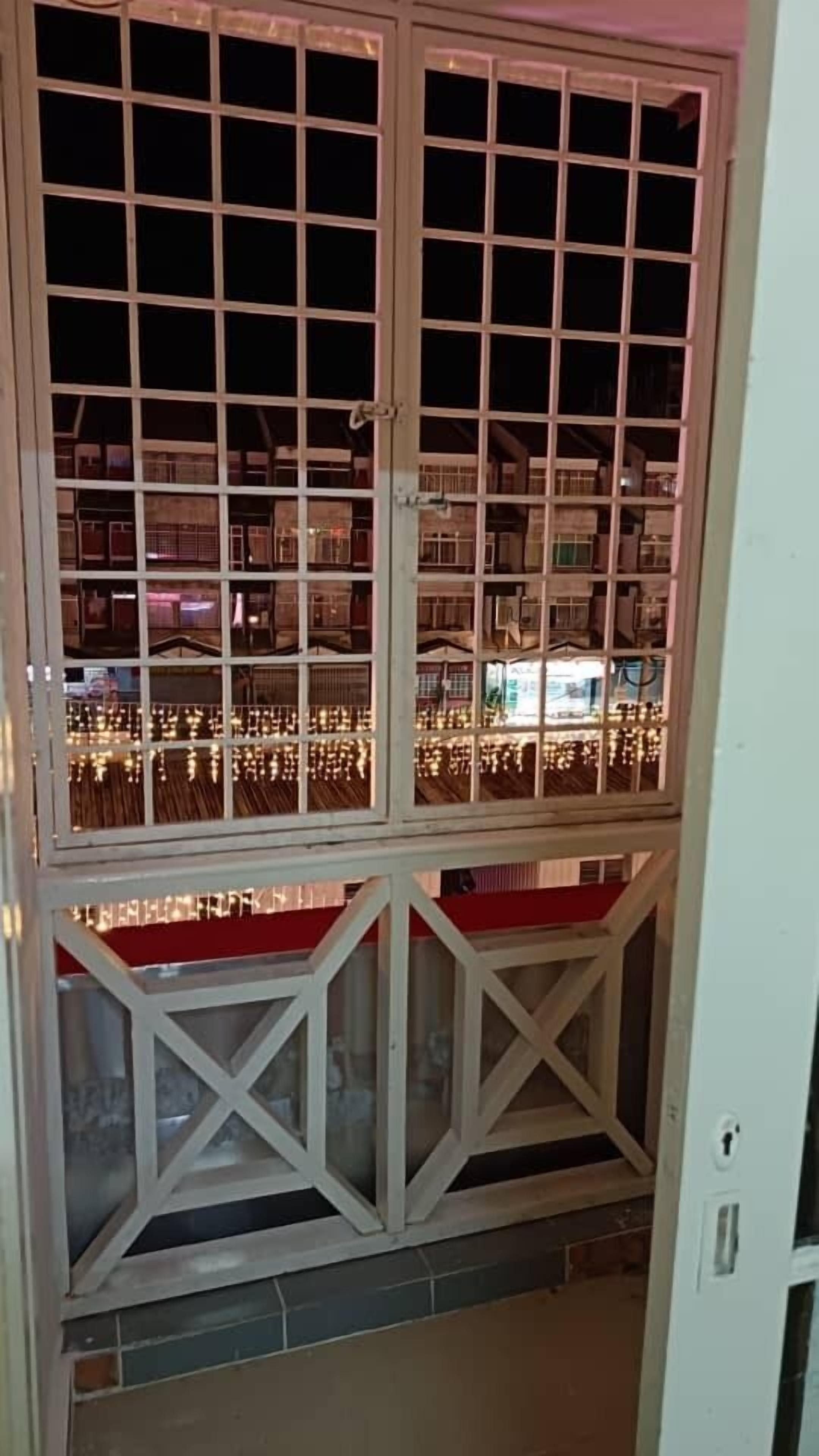 Vista attraverso una finestra con motivi a griglia, che mostra un edificio con diversi piani e una zona con tappeto rosso.