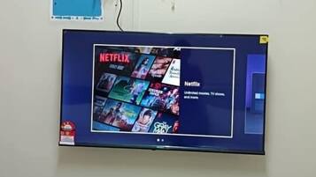 Una TV a parete con contenuti Netflix, una ventola a parete e una ciabatta con cavi.