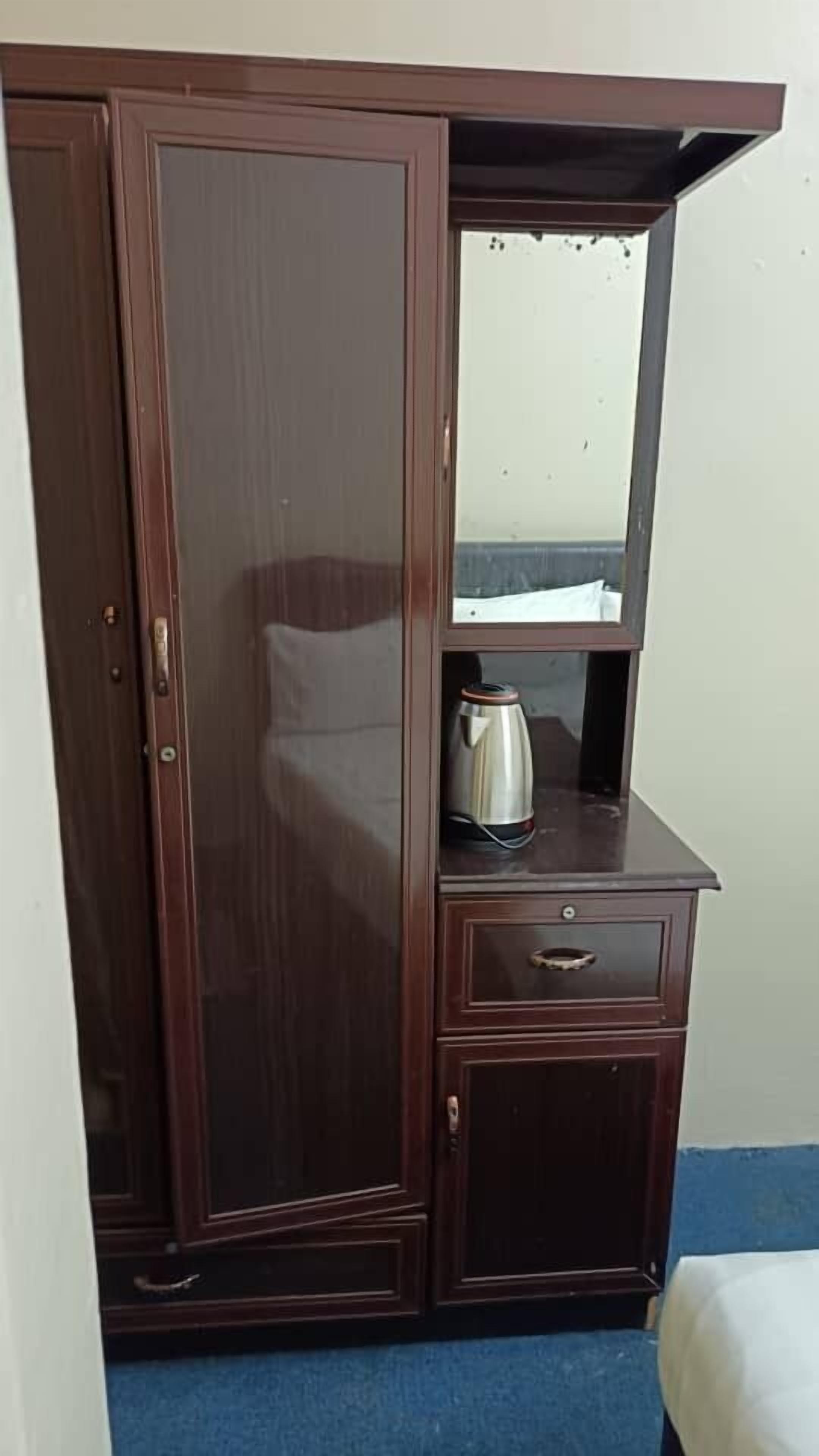 A wooden wardrobe with a mirror, a kettle, and a small drawer.