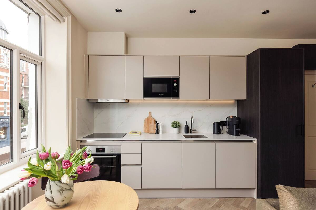 A modern kitchen with a built-in microwave, a wooden cutting board, and a coffee machine.