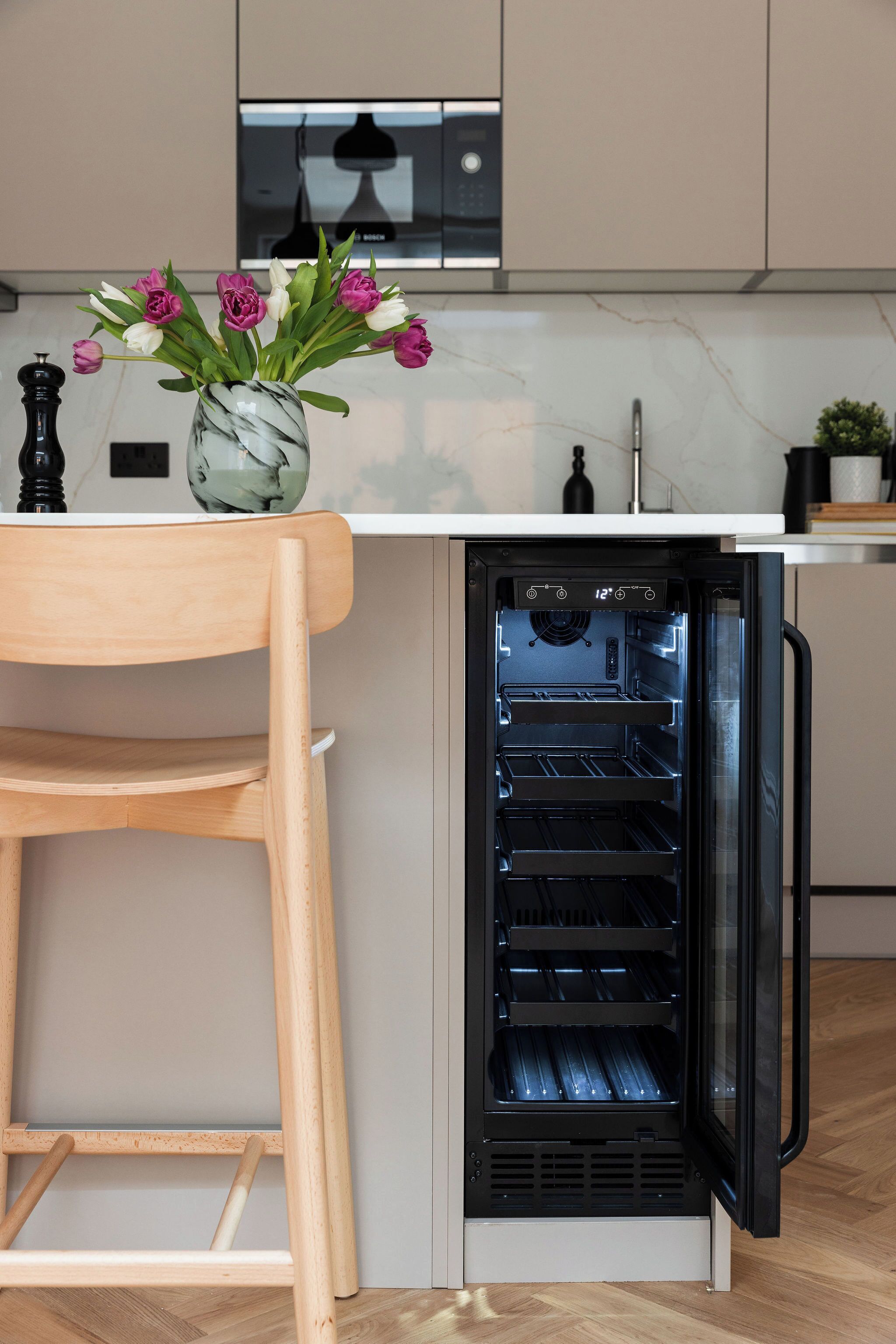 A kitchen with a built-in oven, a wooden chair, and a vase with flowers on the counter.