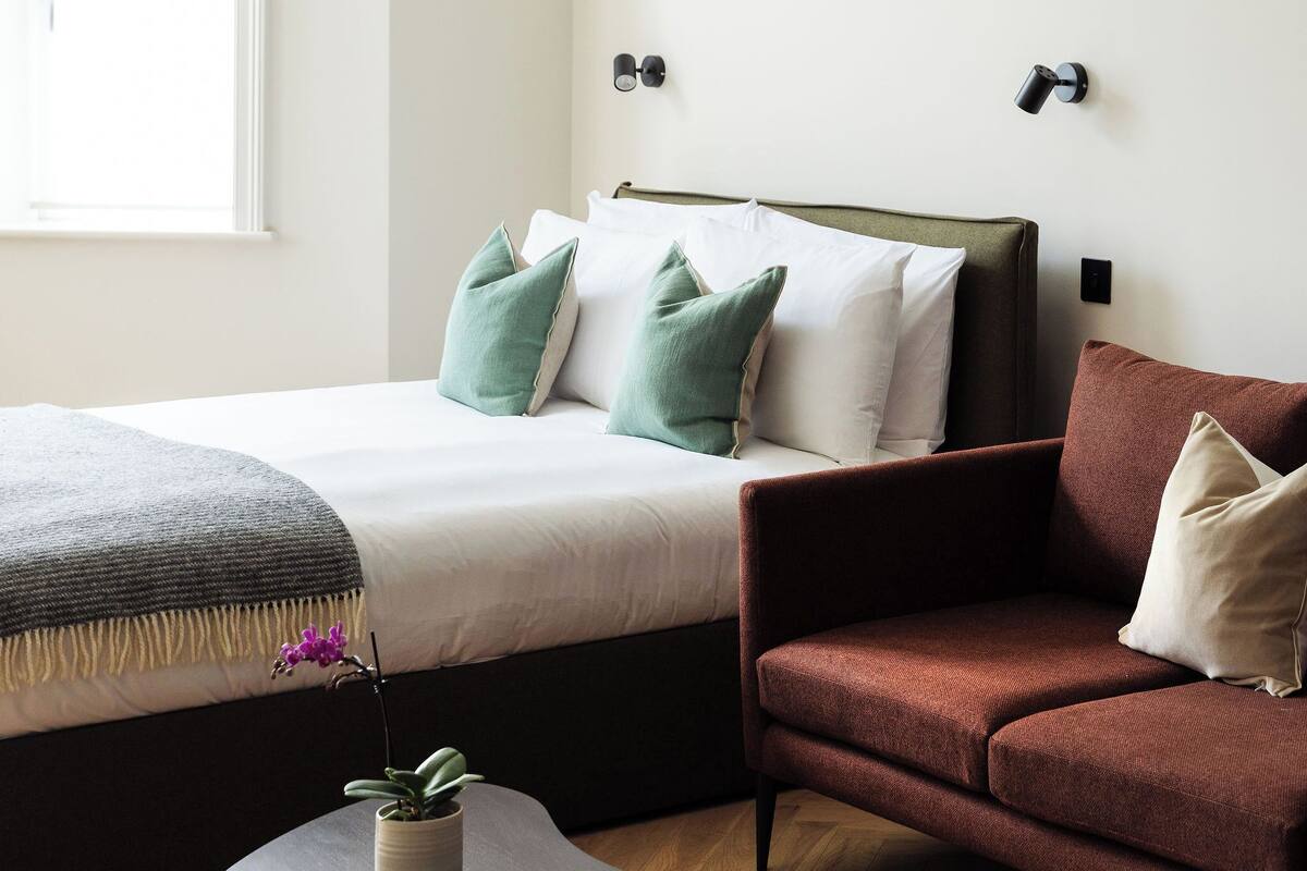 A modern bedroom with a bed, two sofas, a round coffee table, and a potted plant.