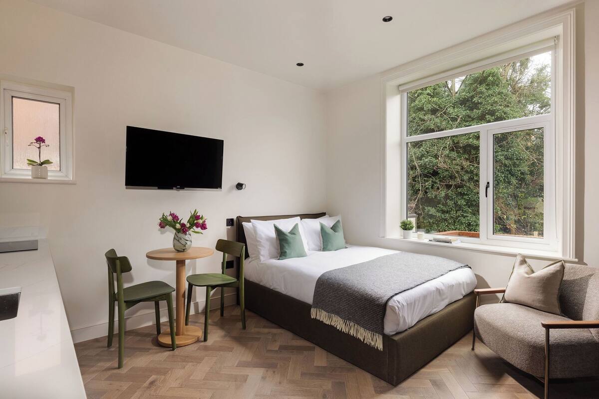 A modern bedroom with a bed, a TV, a window, and a small table with chairs.