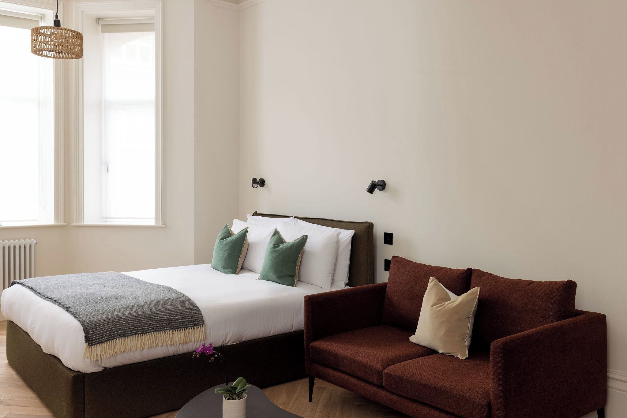 Une chambre à coucher avec un lit, un canapé marron, un luminaire suspendu et une fenêtre.