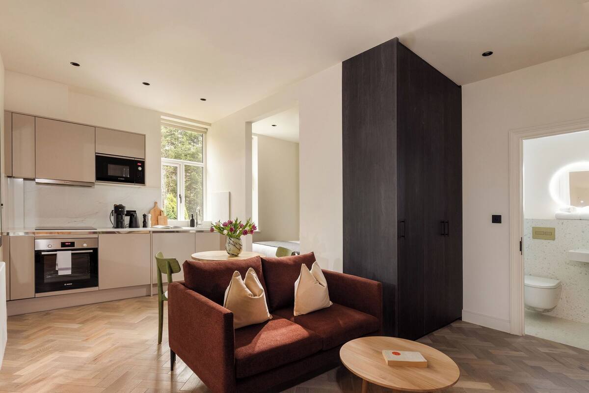 A modern kitchen with built-in appliances, a dining area with a sofa and table, and a dark accent wall.