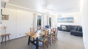 Un salon moderne avec un coin repas, comprenant une table en bois, des chaises, un canapé et un ventilateur de plafond.