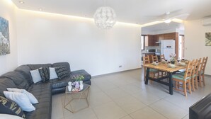 Un salon moderne avec un canapé d’angle, une table à manger avec des chaises et un lustre.