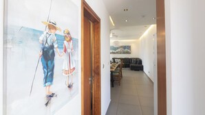 Un couloir avec une porte en bois, un coin repas avec une table et des chaises, et un salon avec un canapé et un tableau au mur.