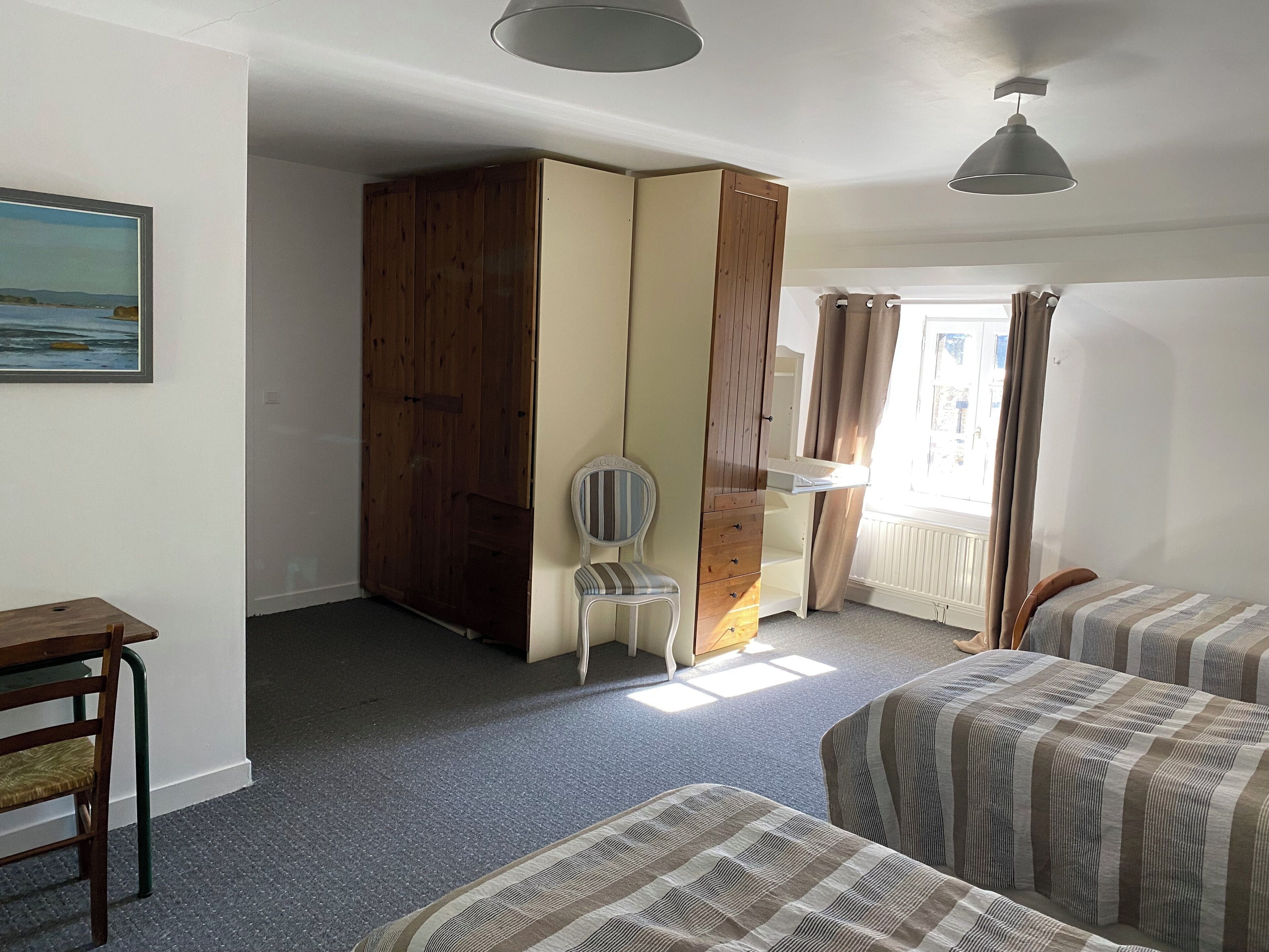 Een slaapkamer met twee bedden, een houten garderobe, een stoel en een bureau.